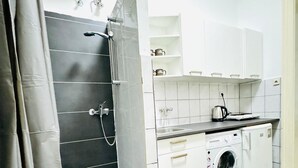 Ett kompakt kök med inbyggd tvätt- och torkmaskin, en duschhörna och en liten arbetsbänk med en vattenkokare.