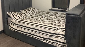 Un lit avec une couverture à rayures, une tête de lit sombre et une petite table de chevet.