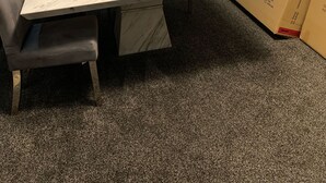 Une pièce avec une table en marbre, des chaises grises, une fenêtre et des cartons.