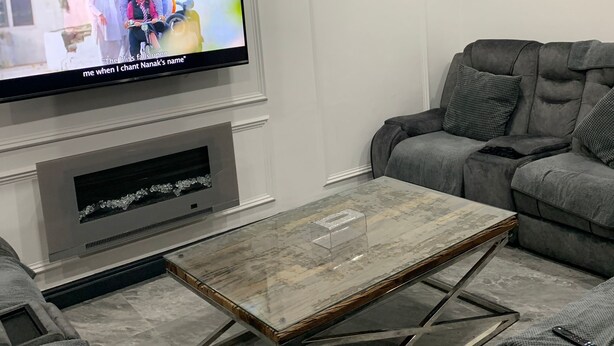 Un salon moderne avec un téléviseur à écran plat fixé au mur, un canapé gris et une table basse en marbre.