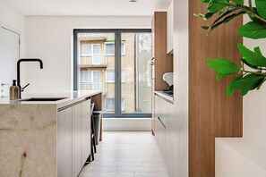 Una cucina moderna con un piano di lavoro in marmo, mobili in legno e vista su un edificio residenziale attraverso una porta in vetro.
