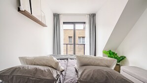 Ein Schlafzimmer mit Bett, Kissen, einem Fenster und einer Pflanze.