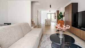 Ein modernes Wohnzimmer mit Sofa, Couchtisch und Fernseher. Eine Treppe führt in einen anderen Raum.
