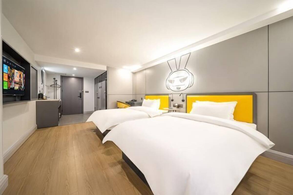 A hotel room with two beds, a TV, a desk, and a bathroom.