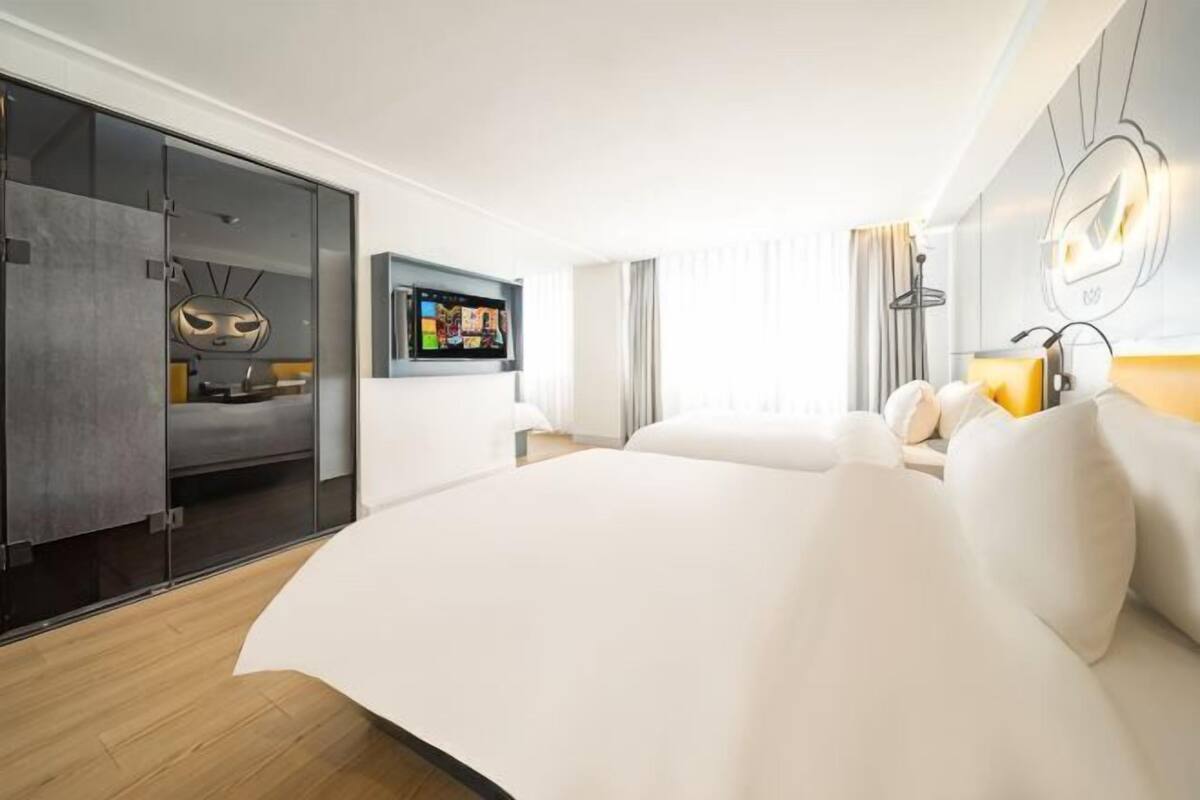 A modern hotel room with a large bed, a TV, a seating area, and a sliding door closet.