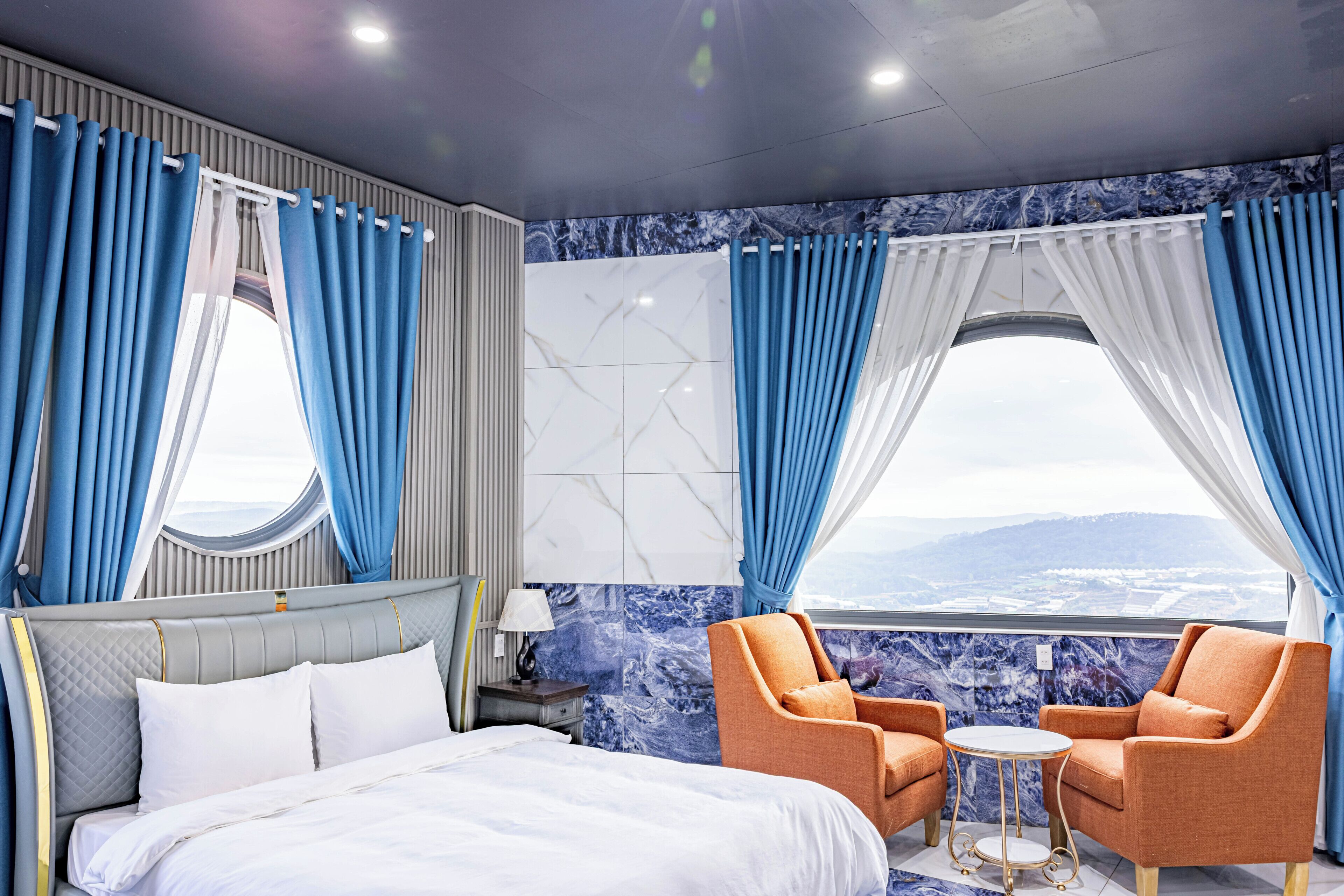A hotel room with a bed, two armchairs, a small table, and a view of the mountains.