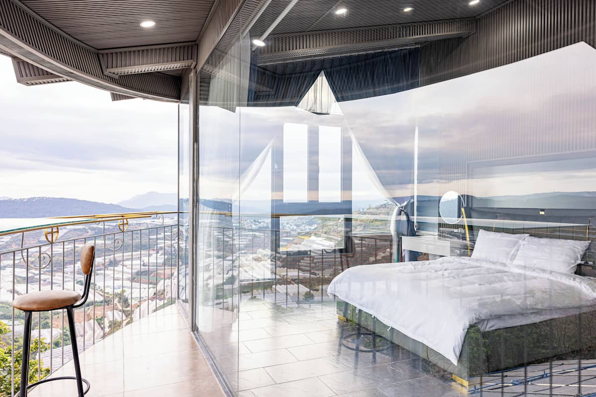 A bedroom with a bed, a chair, and a balcony with a view.