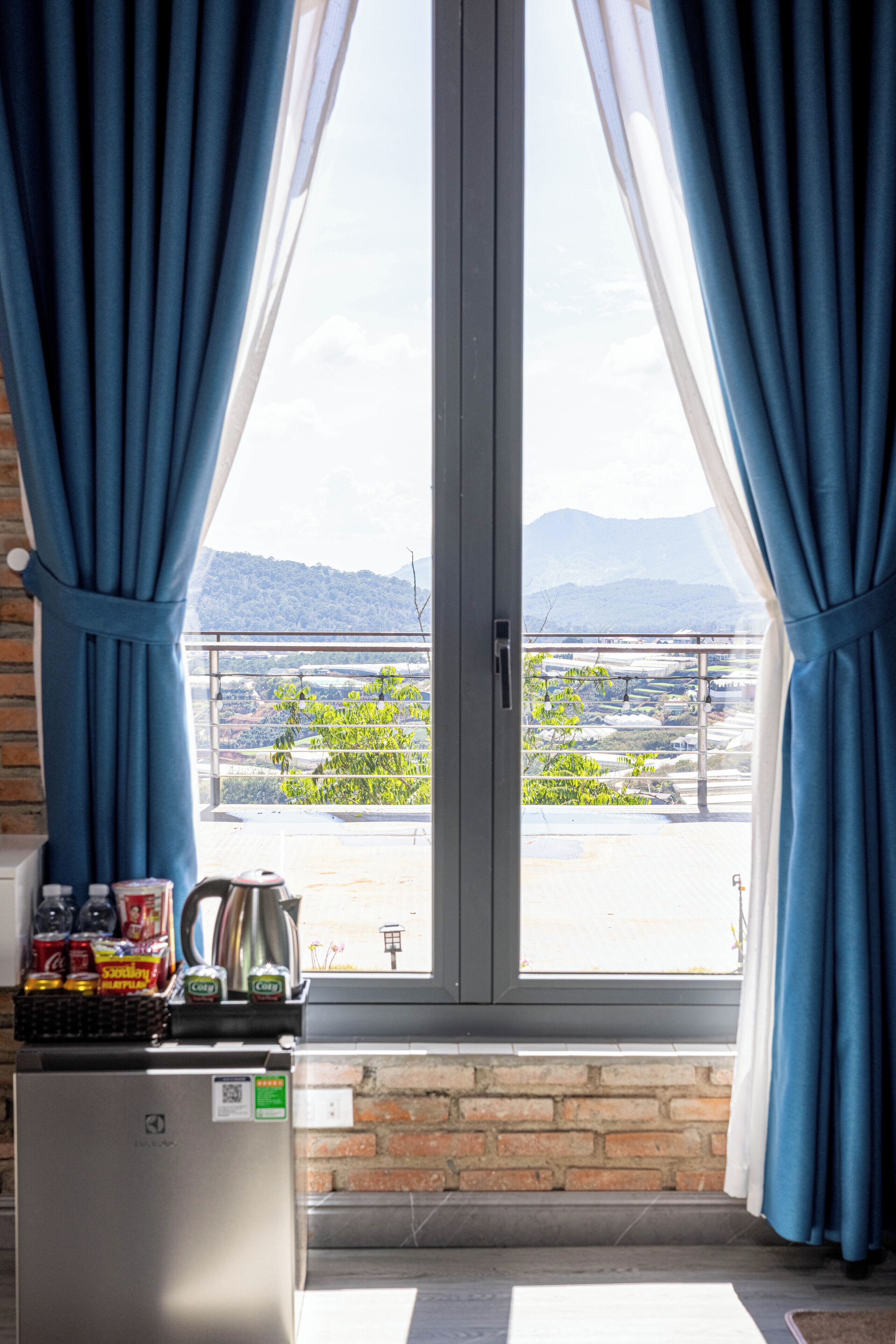 A balcony with a view of a mountainous landscape, a refrigerator with snacks, and a kettle.