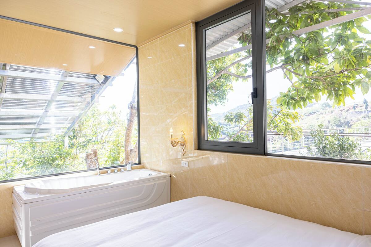 A hotel room with a large window, a bathtub, and a bed.