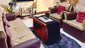 Una sala de estar con un sofá, una mesa de centro con una computadora portátil, un televisor, un ventilador y una escalera.