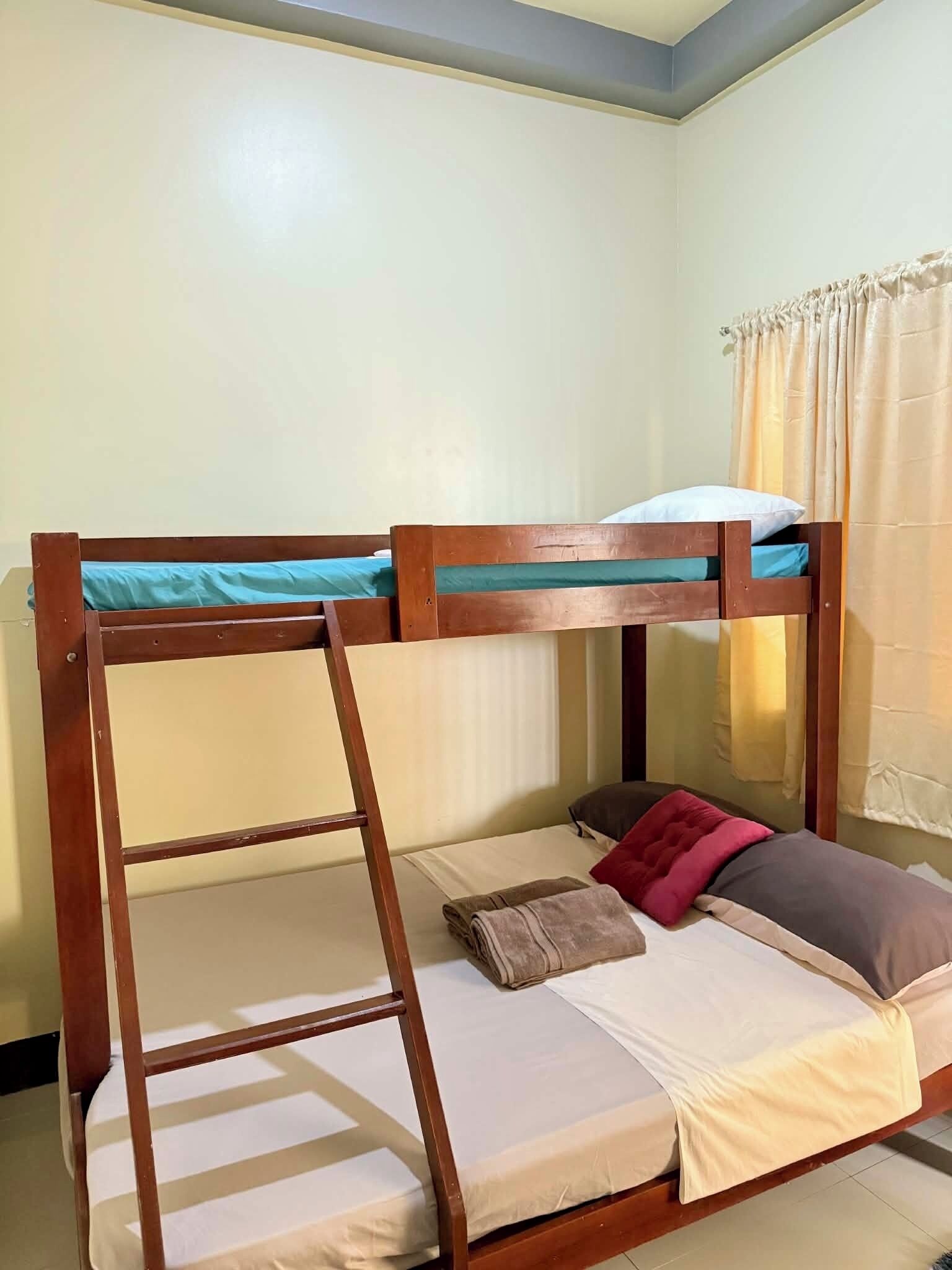 A bunk bed with a ladder, a single bed with pillows, and a curtain.