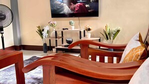 Una sala de estar con un sofá de madera, un televisor en la pared, una mesita con una planta en maceta y una lámpara de pie.