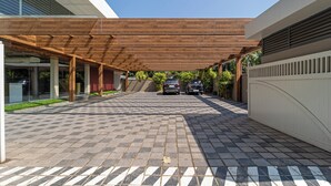 Ett takförsett utomhusområde med ett klinkergolv, två parkerade bilar och en byggnad med modern design.