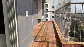 A narrow balcony with a wooden floor, metal railing, and a view of a cityscape.