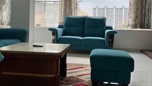 A spacious living room with a large window, a blue sofa, a matching ottoman, and a coffee table.
