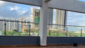 A spacious room with a wooden floor and large windows offering views of a cityscape with high-rise buildings and construction cranes.