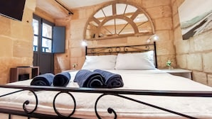 A cozy room with a stone wall, a large bed with rolled towels, a wooden arched window, and a flat-screen TV on the wall. - Historic 300 Years Townhouse in Birgu, Vittoriosa (Birgu)