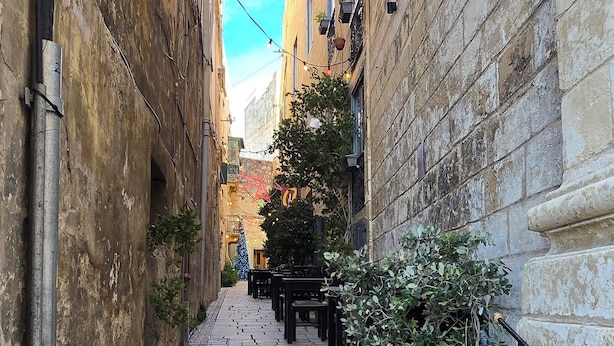 A narrow stone-paved alleyway flanked by buildings with outdoor seating and potted plants. - Historic 300 Years Townhouse in Birgu, Vittoriosa (Birgu)