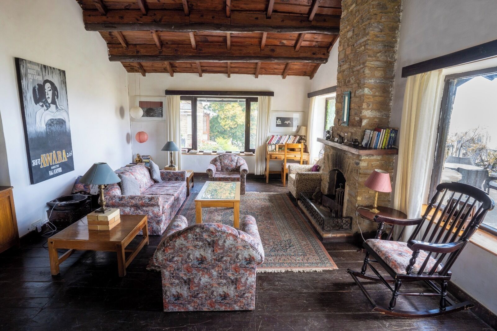 A cozy living room with a stone fireplace, wooden furniture, and a view of the outdoors.