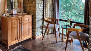Una habitación rústica con pared de piedra, vigas de madera en el techo, un armario de madera, un espejo, una silla, una pequeña mesa con un jarrón y vistas a la vegetación.