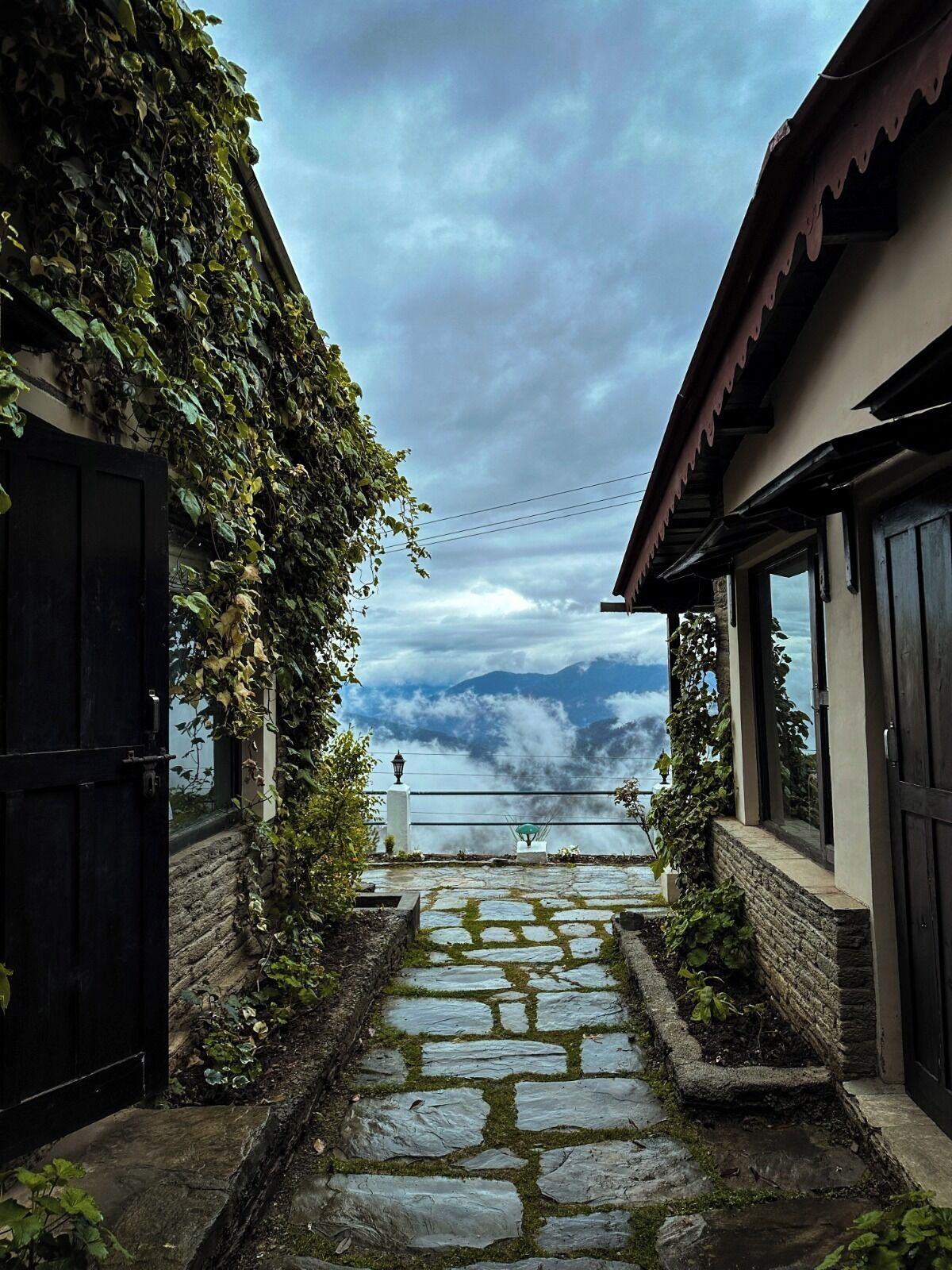 A stone pathway leading to a gate with a view of mountains and clouds.