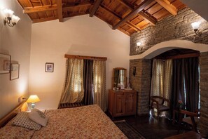 Un dormitorio acogedor con techo de madera, paredes de piedra, una cama con ropa de cama estampada, un aparador y una silla.