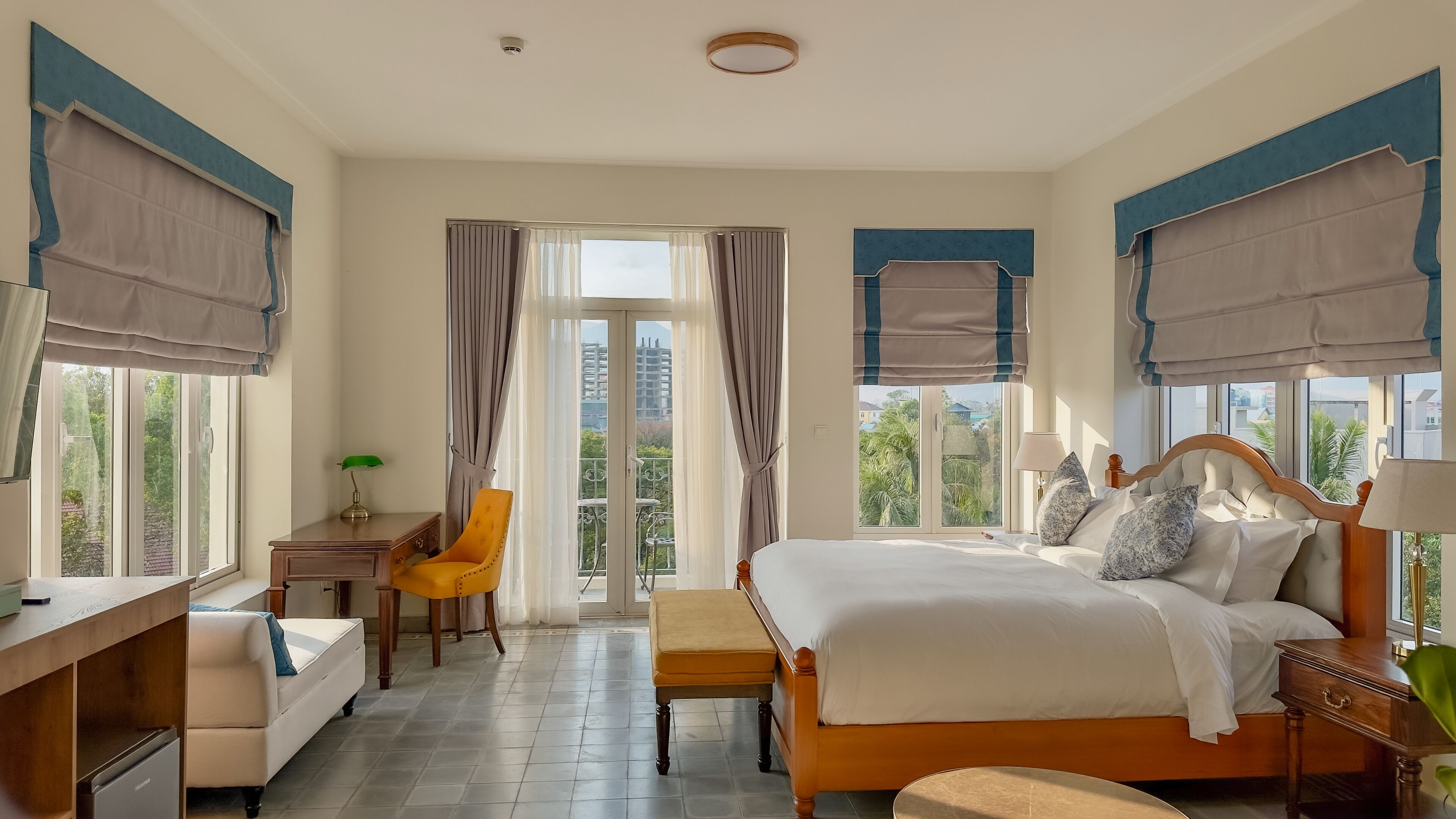 A hotel room with a bed, bedside table, chair, desk, and a view of the outside.