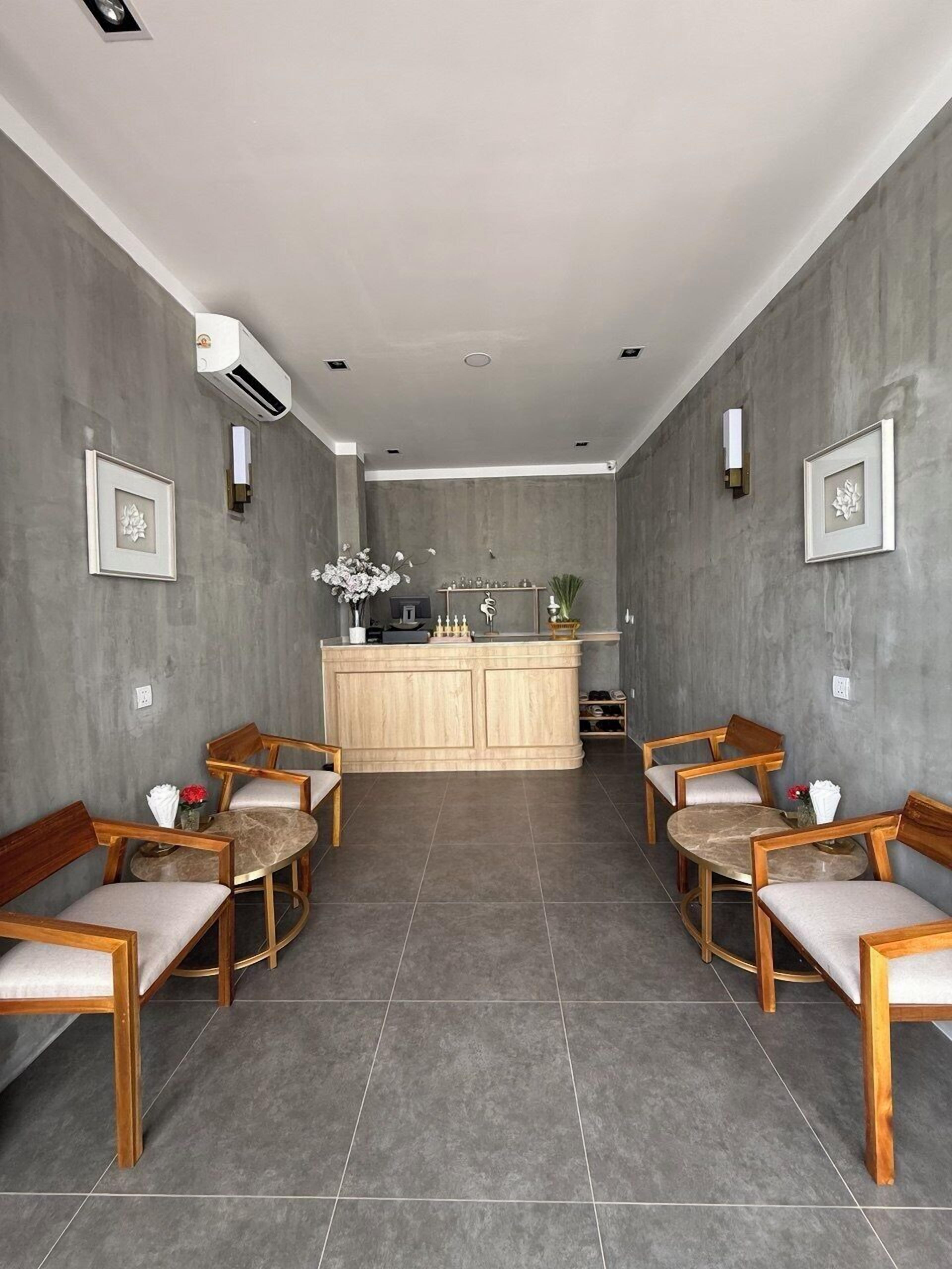 Un interior moderno con una barra de madera central, dos zonas de estar con sillas de madera, suelo de baldosas grises y paredes grises.