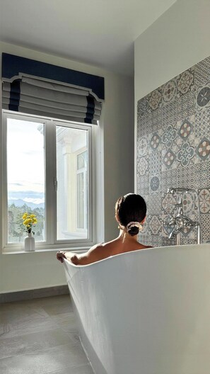 Ein Badezimmer mit Badewanne, einem Fenster mit Aussicht und Wandfliesen mit Muster.