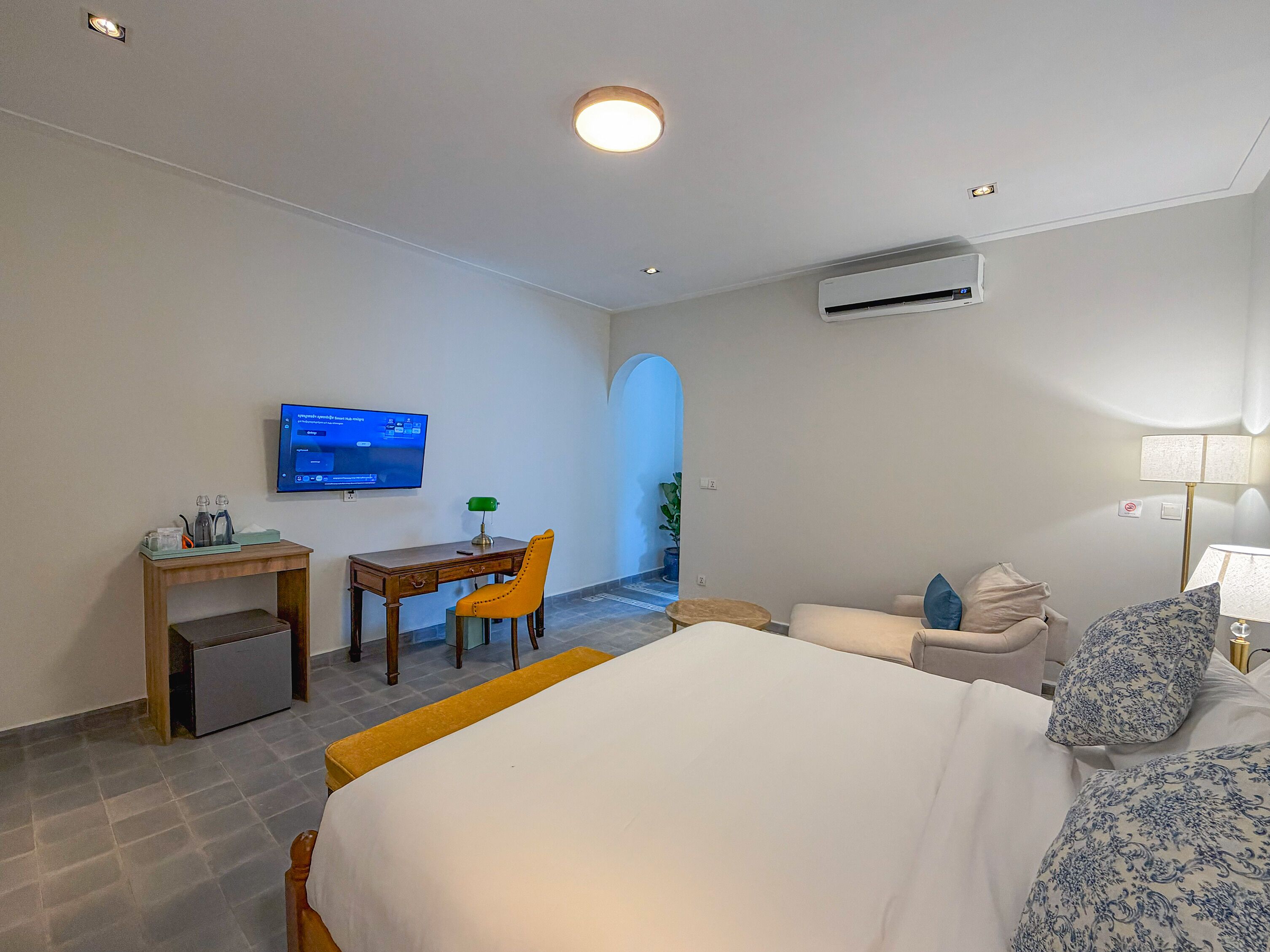 Ein Hotelzimmer mit Bett, Schreibtisch mit Stuhl, Fernseher, Klimaanlage und Lampe.