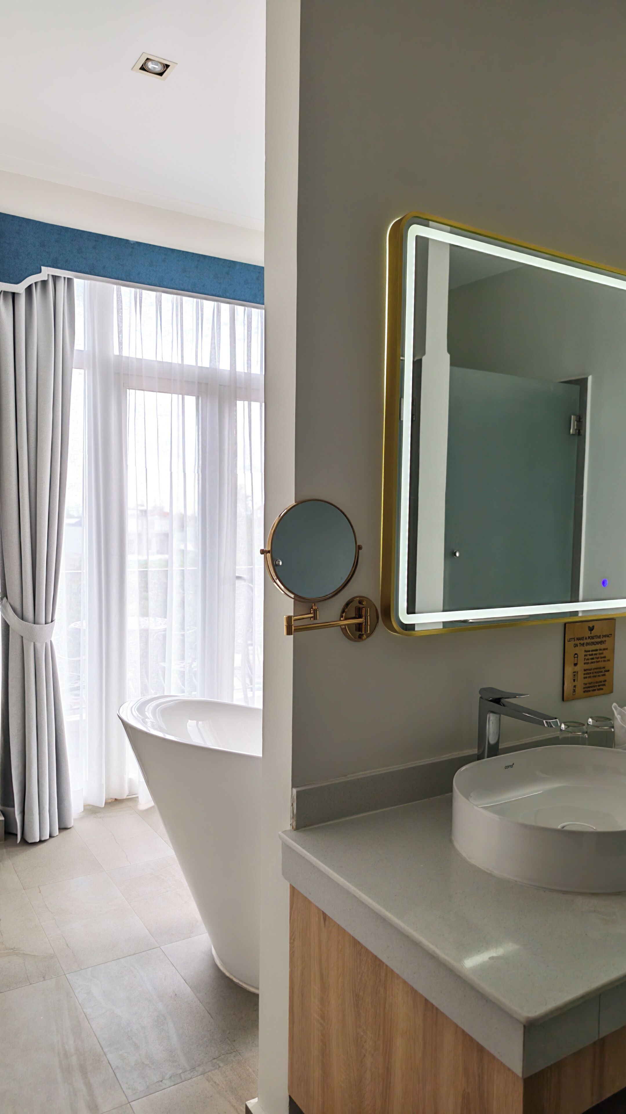 A modern bathroom with a freestanding bathtub, a round mirror with a gold frame, and a large rectangular mirror above the sink.