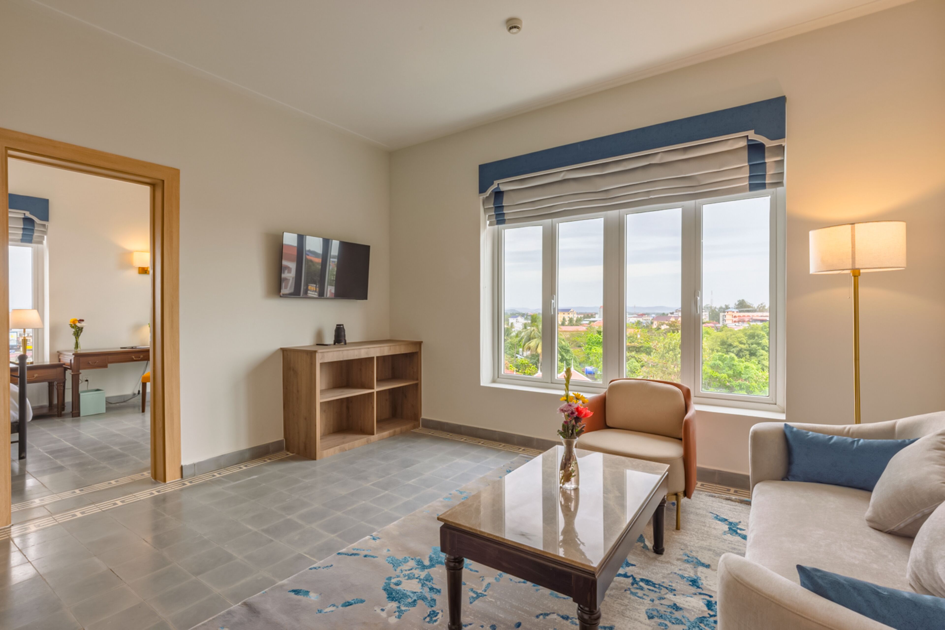 A spacious living room with a large window, a sofa, a coffee table, and a bookshelf.