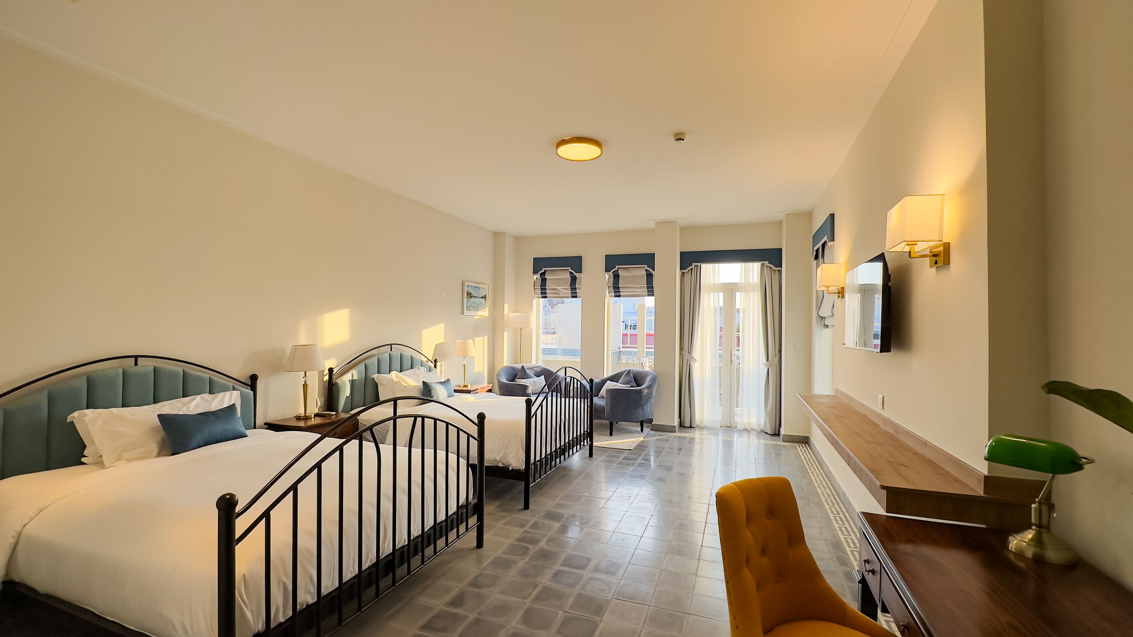 A hotel room with a bed, two bedside tables, a chair, a desk, a mirror, and a window with curtains.