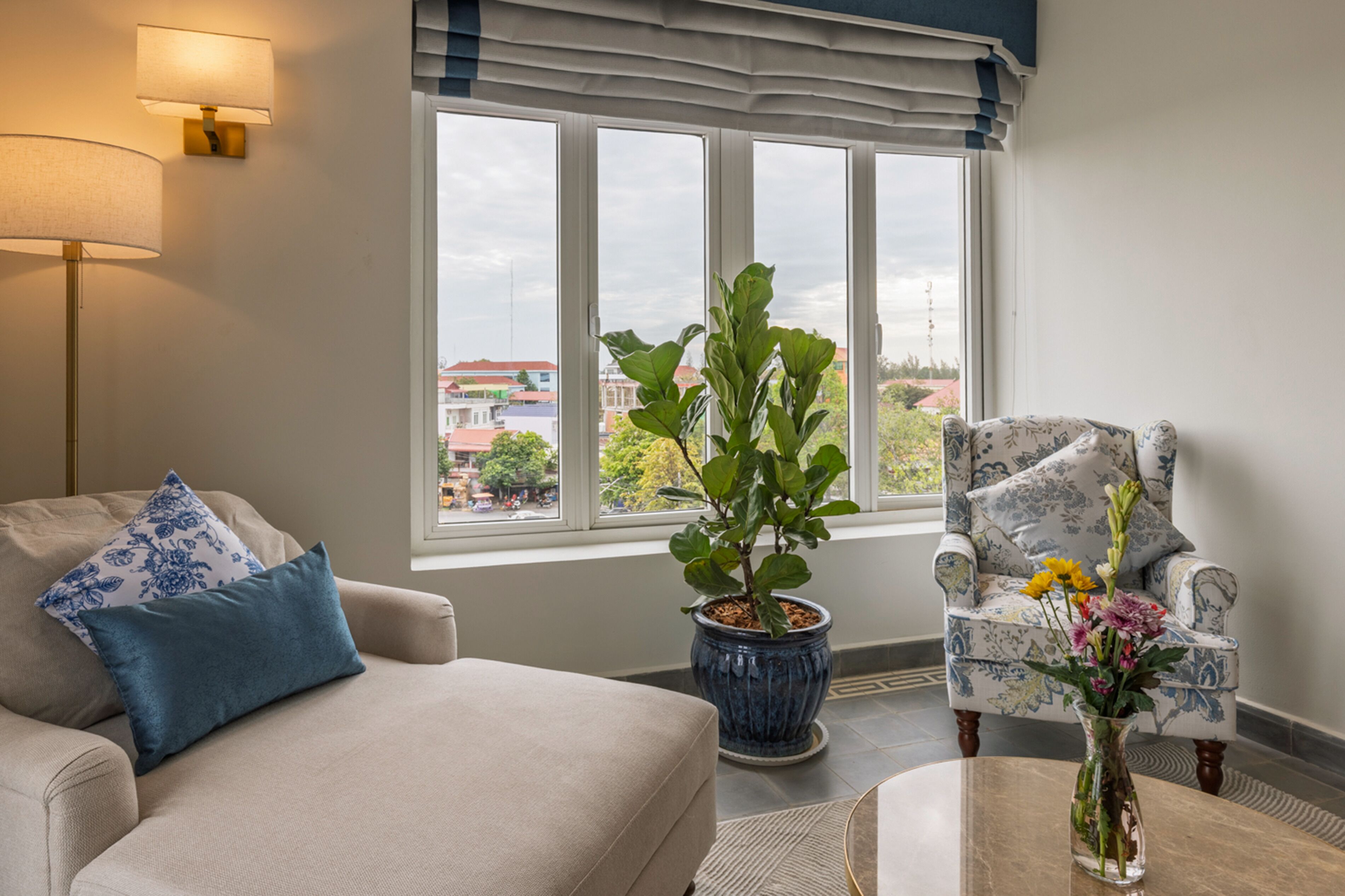 Habitación con sofá, sillón y planta en maceta junto a una ventana con vista a la ciudad.