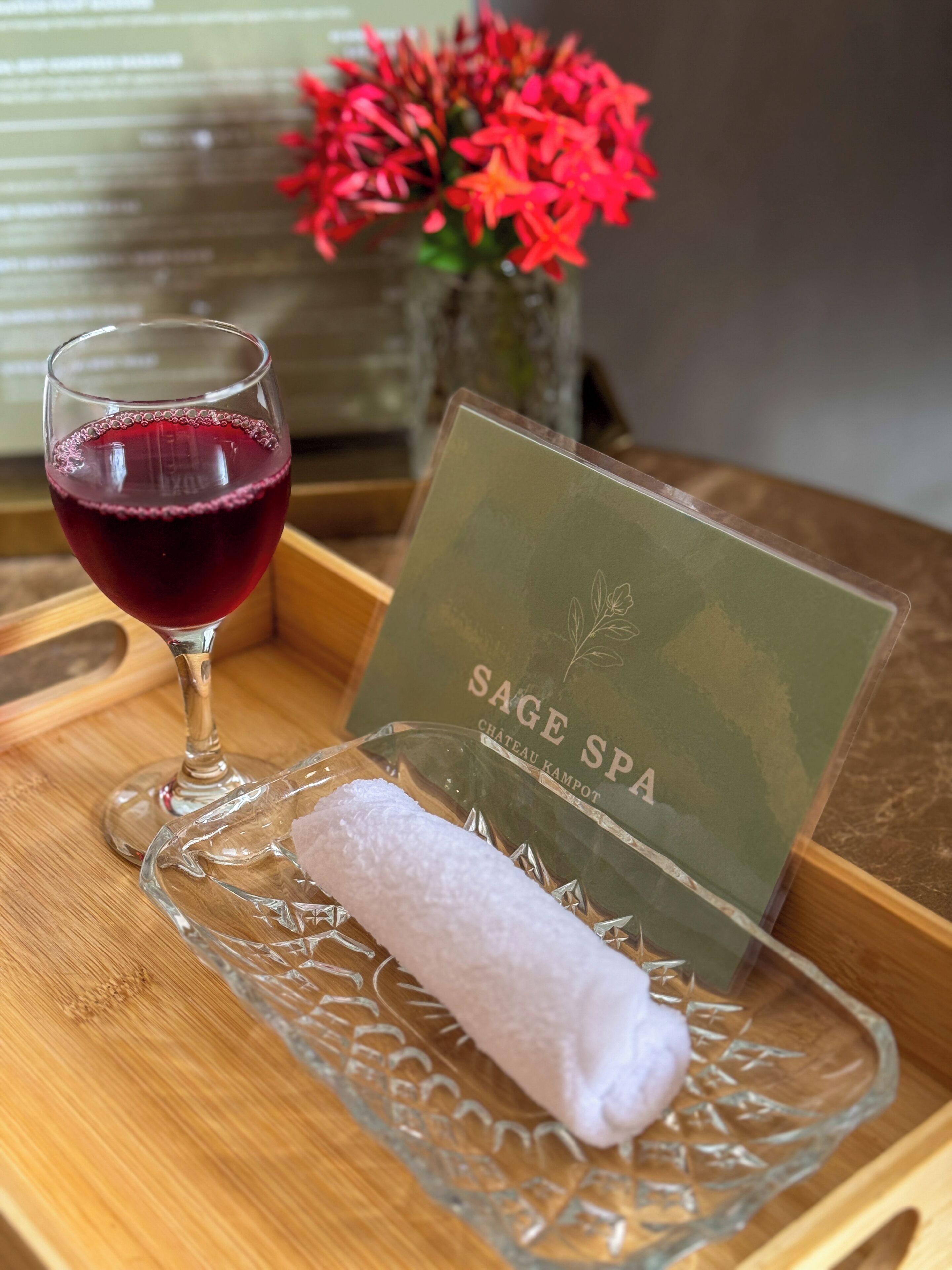 Una copa de vino tinto, una toalla enrollada y una tarjeta sobre una bandeja de madera.