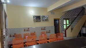 Une salle de conférence avec une longue table et des chaises orange, un mur recouvert de carreaux formant un motif géométrique, et un escalier au motif à carreaux noirs et blancs.