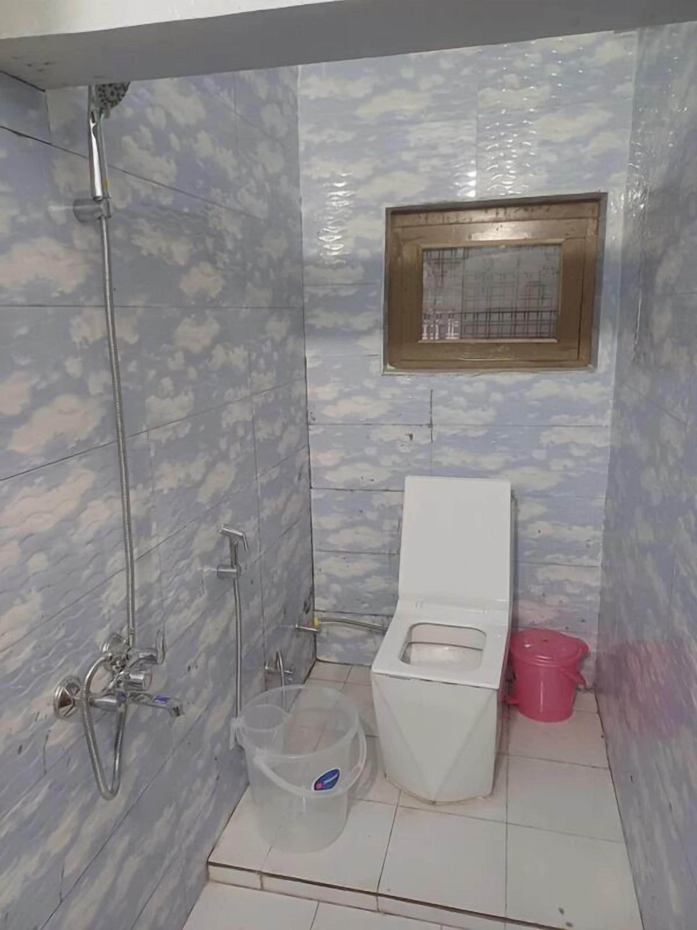 A bathroom with a shower, toilet, and a small window.