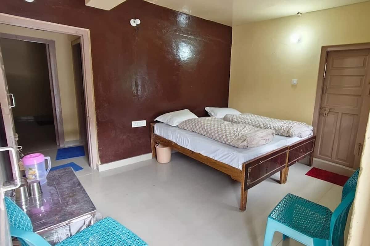 A bedroom with a wooden bed, a small table with a pink water bottle, and two blue chairs.