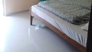 Une chambre à coucher avec un lit, deux chaises, une fenêtre aux vitres vertes et un sol carrelé.