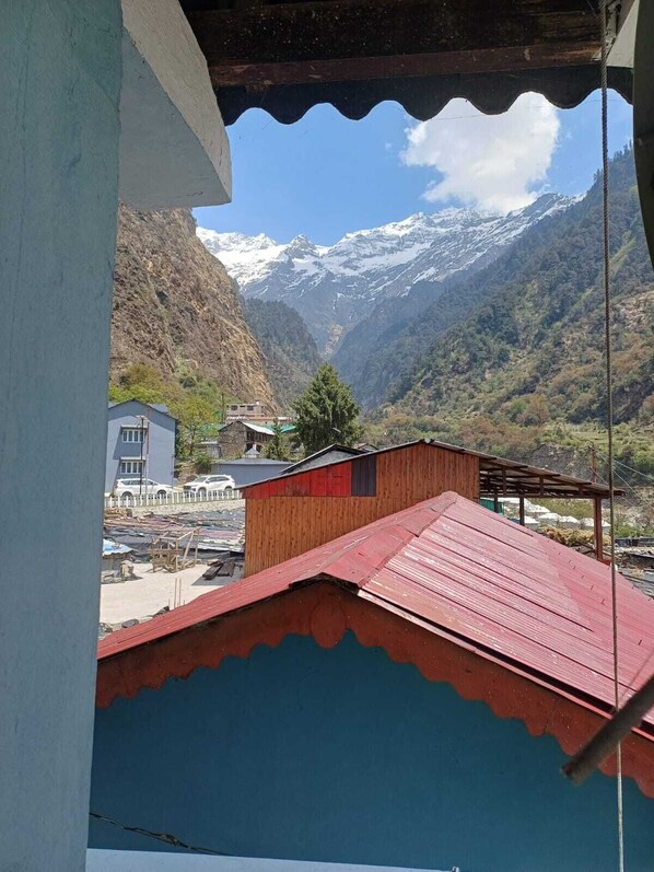 A mountainous landscape with snow-capped peaks, a valley, and a view of a building with a red roof.