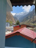 Un paisaje montañoso con picos nevados, un valle y una vista de un edificio con techo rojo.