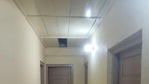 Un couloir étroit au sol carrelé, une porte en bois au fond et un luminaire au plafond.