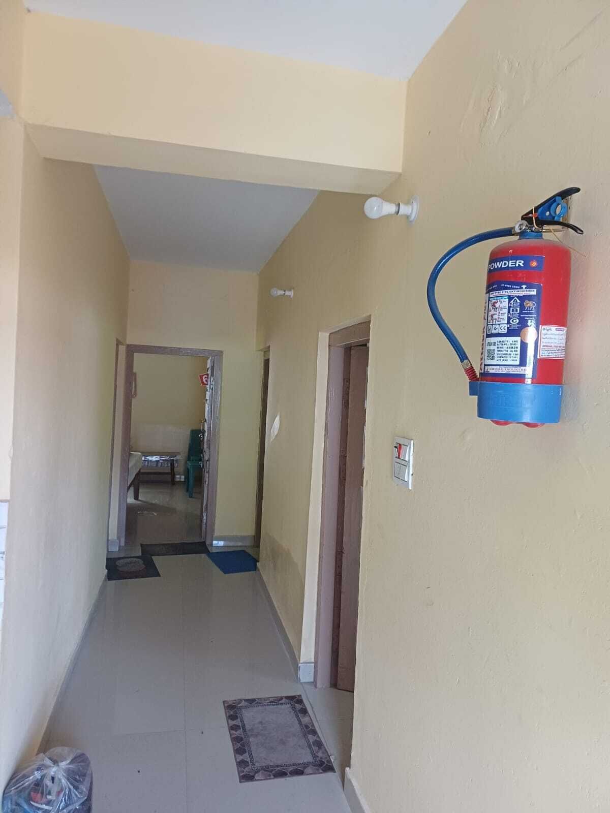 A hallway with a fire extinguisher mounted on the wall, a door at the end, and a small rug on the floor.