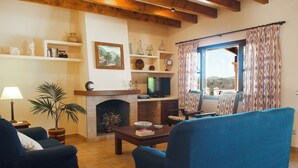 Una sala de estar con chimenea, televisor y vistas al exterior a través de un ventanal.