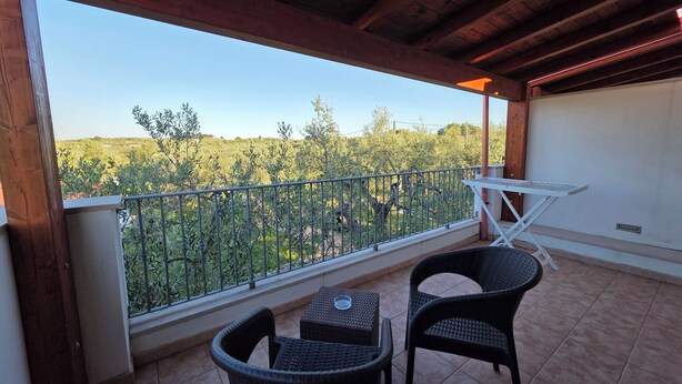 Ein Balkon mit Korbstühlen, einem kleinen Tisch und Blick auf eine grüne Landschaft.