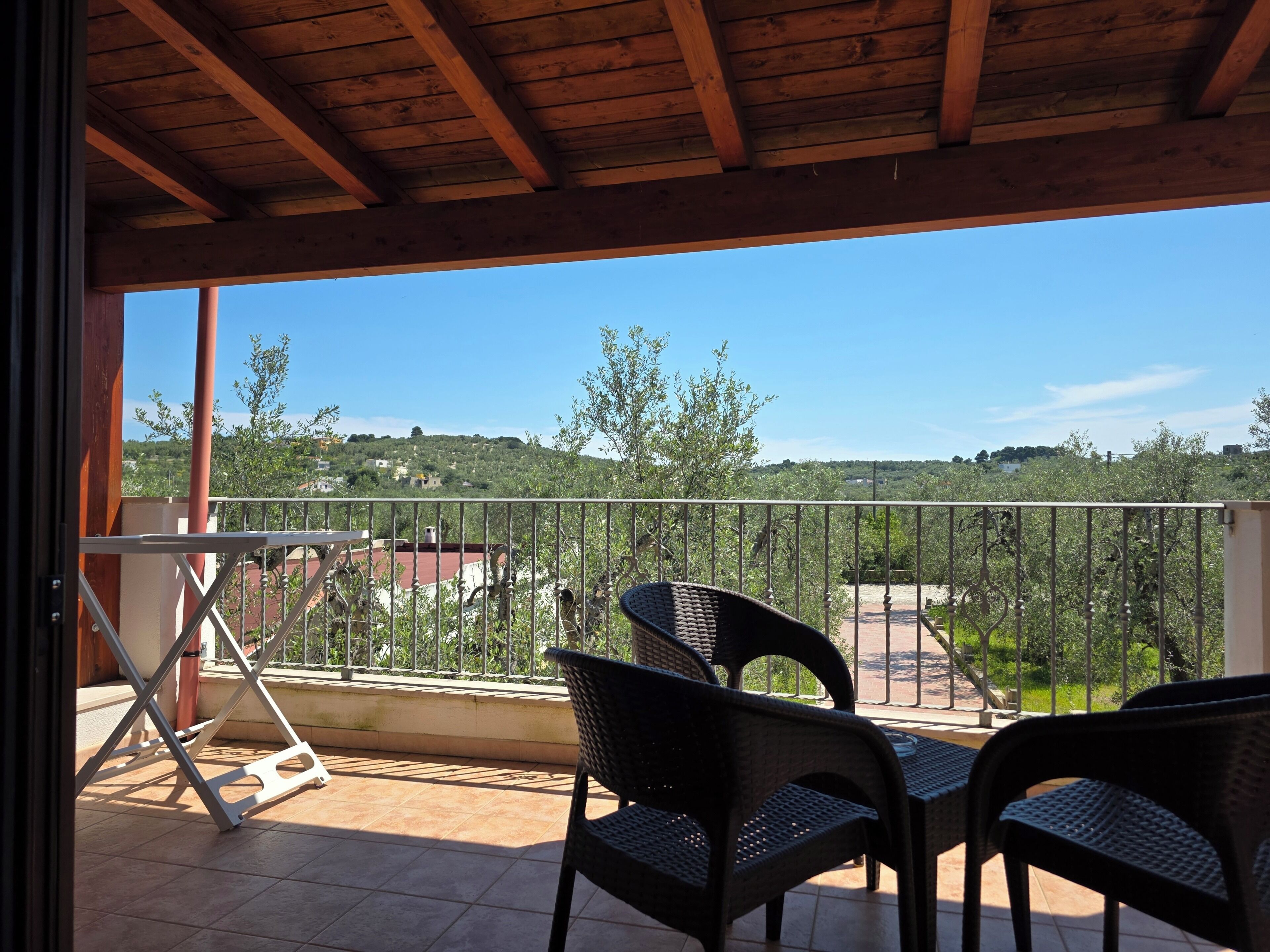 A balcony with a view of a hilly landscape, a metal railing, and two wicker chairs.