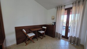 Ein Zimmer mit einem Holztisch, zwei Stühlen, einer Lampe und Blick ins Freie durch eine Tür.
