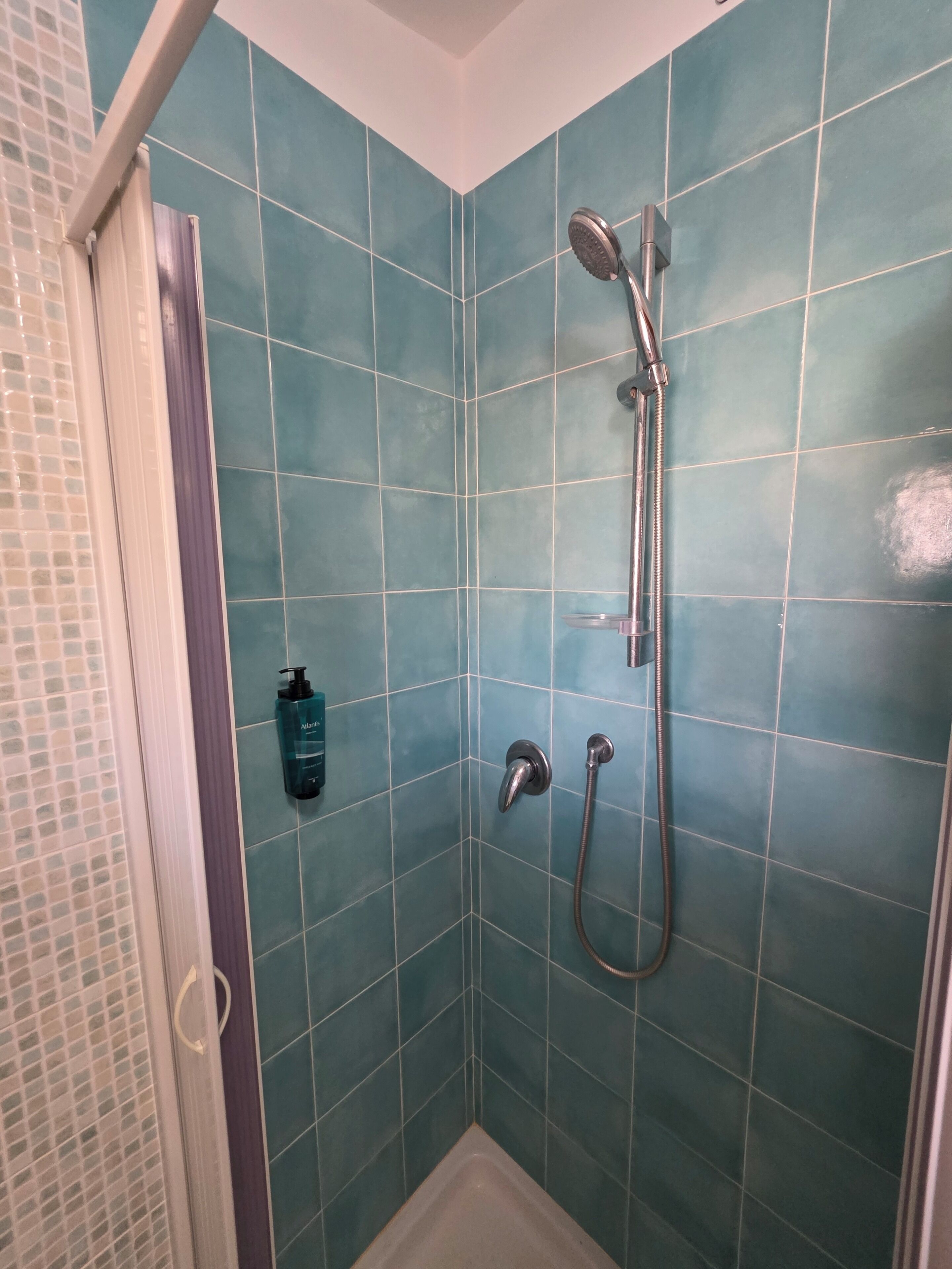 Un espace douche avec des carreaux de couleur turquoise, une douchette à main et un robinet fixé au mur.
