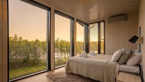 Makuuhuoneessa on suuri ikkuna, sänky, yöpöytä ja näkymä puita kohti.