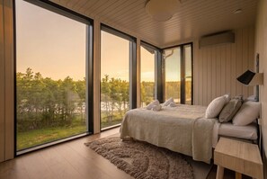 A bedroom with a large window, a bed, a bedside table, and a view of a forest. - Stay   North - Sundet (Kirkkonummi)
